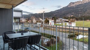 Ein Balkon mit Tisch und Stühlen, der auf Gleise und eine Berglandschaft blickt.