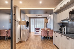 Une cuisine moderne dotée d’un four encastré, un coin repas avec une table et des chaises, et une grande fenêtre agrémentée de rideaux.