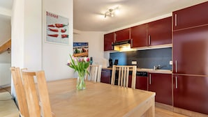 A modern kitchen with wooden cabinets, a dining table with chairs, and a vase with flowers. - Apartment 'Ferienwohnung, 55qm' with Wi-Fi (Neuried)