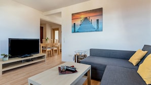 A modern living room with a flat-screen TV, a grey sofa, and a painting of a pier. - Apartment 'Ferienwohnung, 55qm' with Wi-Fi (Neuried)