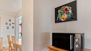 A modern kitchen with a microwave on a wooden stand, a dining area with wooden chairs, and a wall with framed pictures. - Apartment 'Ferienwohnung, 55qm' with Wi-Fi (Neuried)
