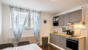 Cozinha com armários cinza, bancada branca, fogão e janela com cortinas estampadas.