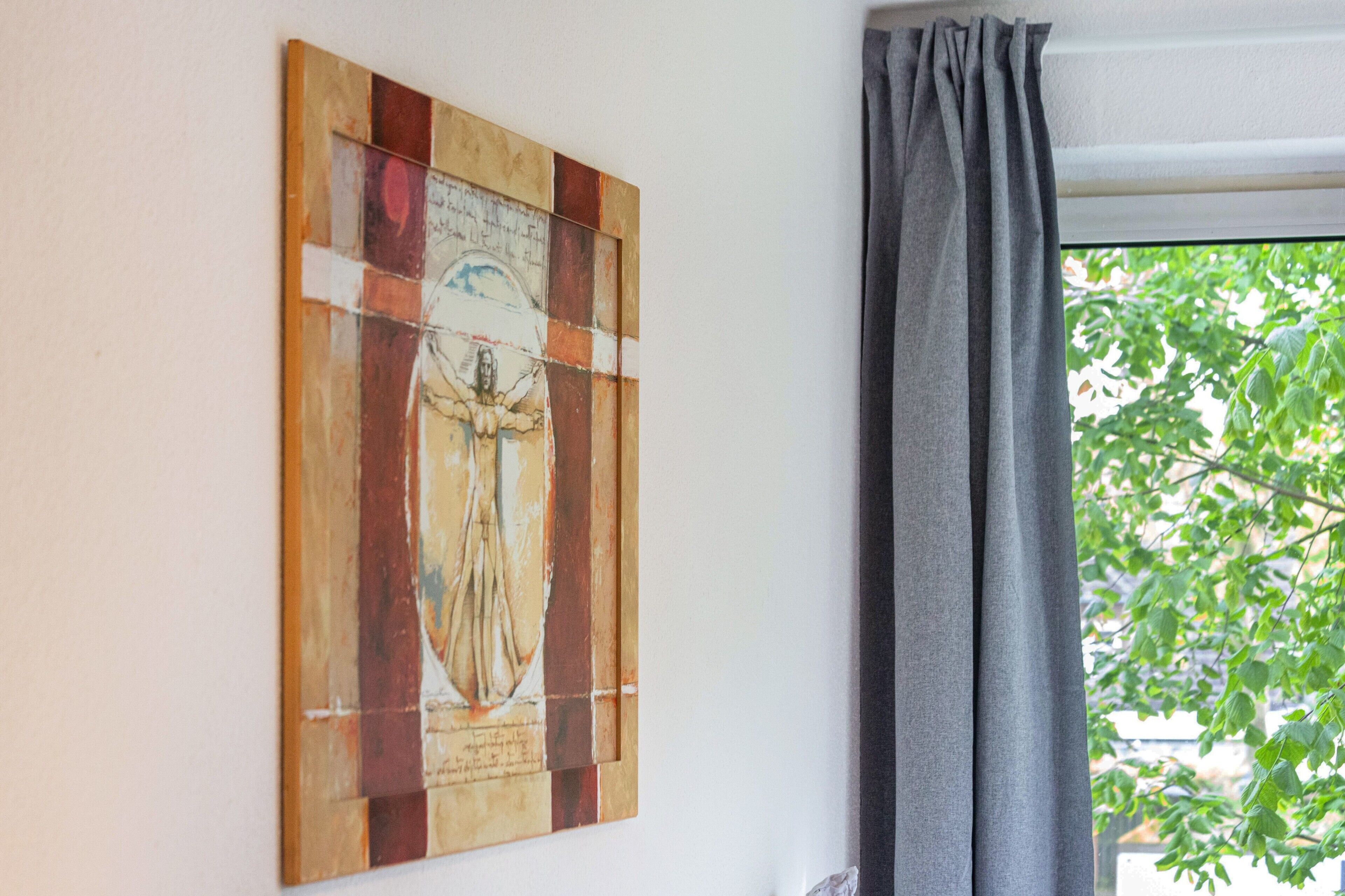 Eine Wand mit einem gerahmten Kunstwerk und einem Fenster mit Vorhang.