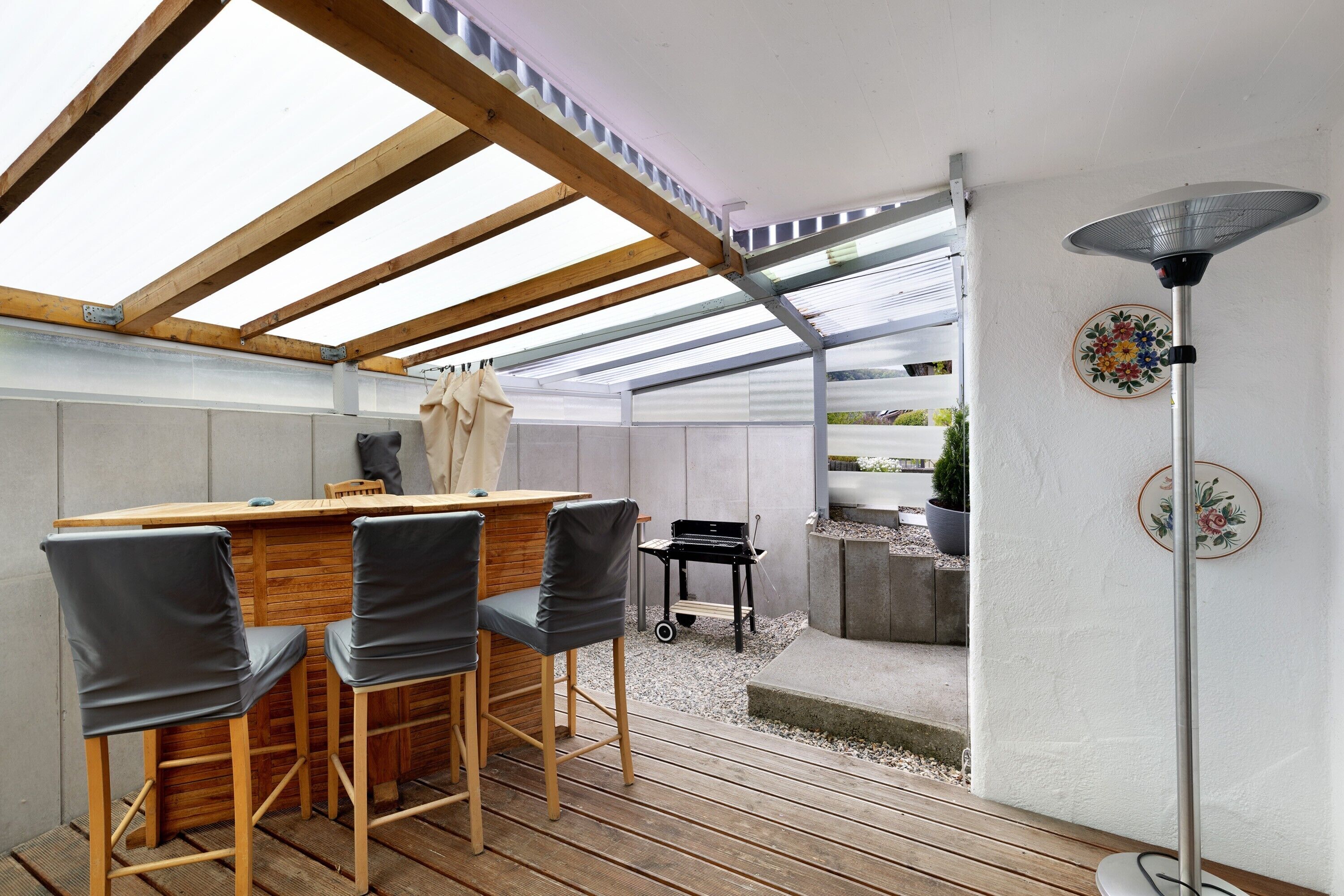 Un espace extérieur abrité, avec une table et des chaises en bois, un barbecue et une lampe sur pied.