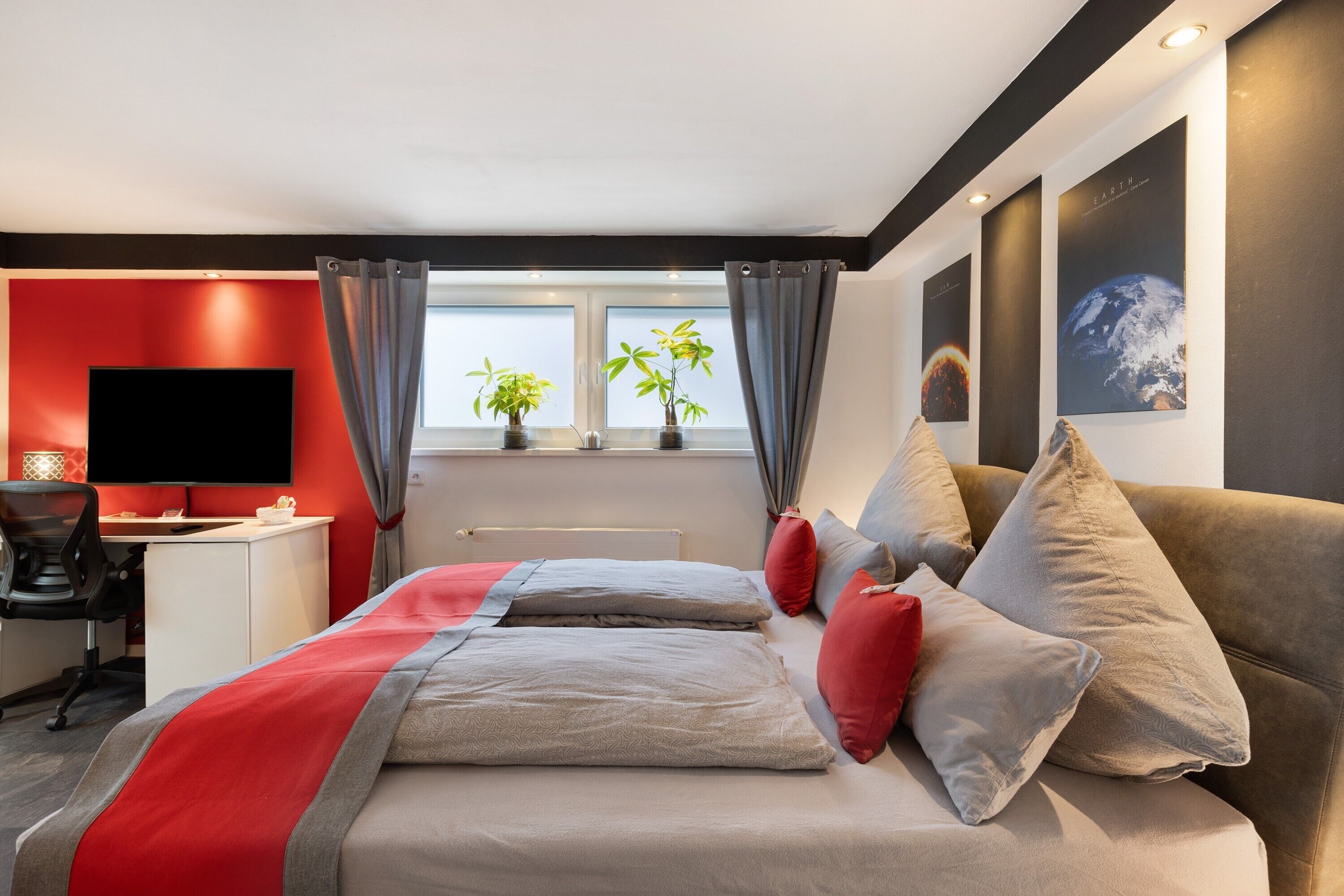 A modern hotel room with a bed, a desk, a television, and two potted plants.
