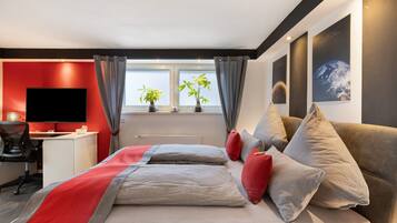 A modern hotel room with a bed, a desk, a television, and two potted plants.