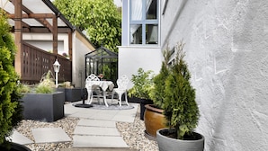 Un'area patio con tavolo e sedie, piante in vaso e una struttura a pergola.