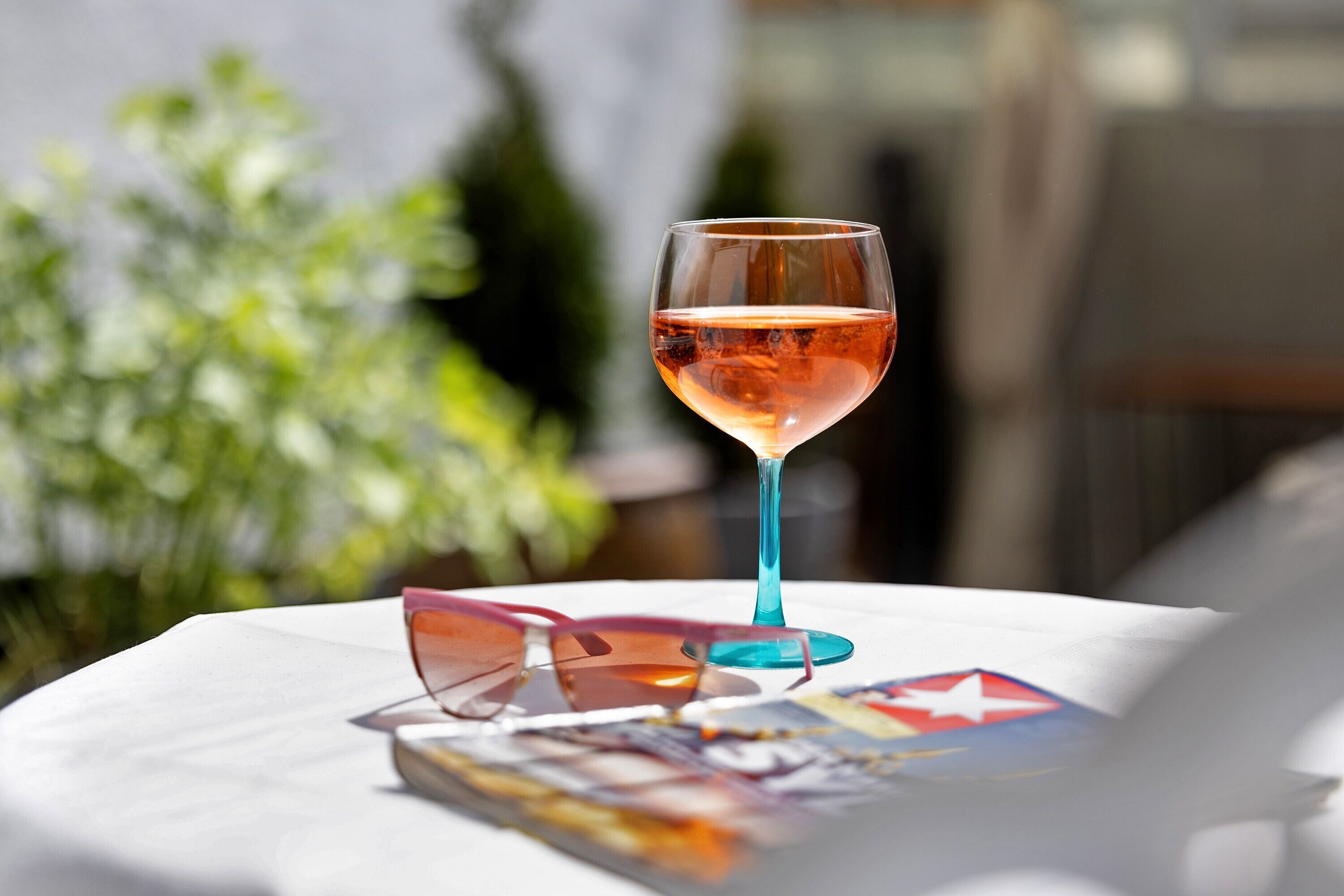 Una mesa con un vaso de líquido rosado, gafas de sol y una revista.