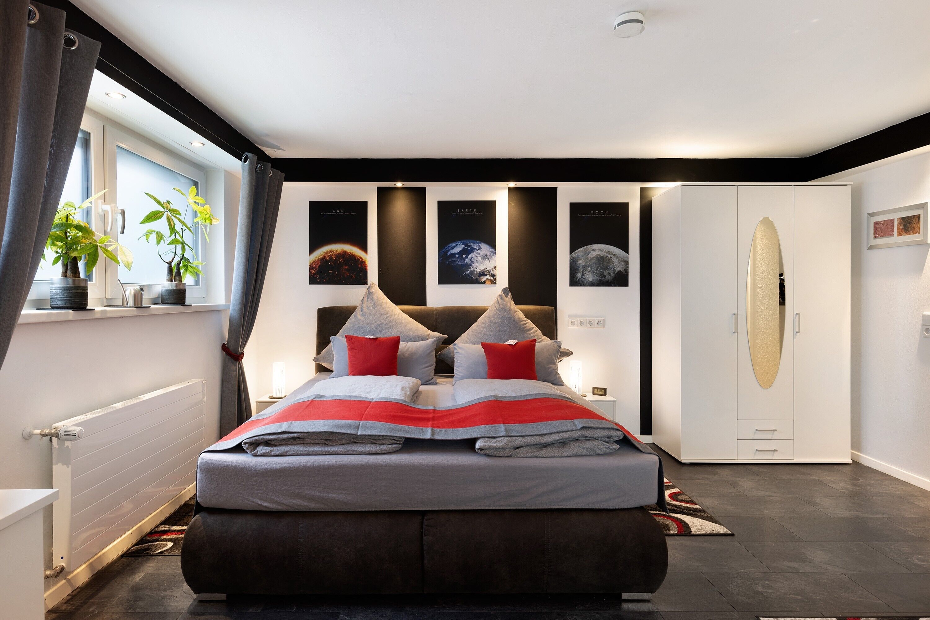 Ein modernes Schlafzimmer mit einem großen Bett, einem Kleiderschrank, einem Heizkörper und einem Fenster mit Vorhängen.