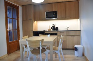 Una cocina compacta con armarios de madera, microondas, lavavajillas y una mesa de comedor con sillas.