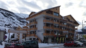 Un hotel de varios pisos con balcones, un telesilla al fondo y un paisaje montañoso cubierto de nieve.