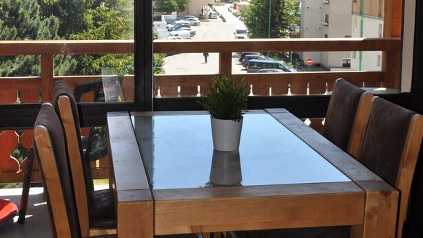 Un restaurante con una mesa y sillas de madera, una planta en maceta y vistas de un pueblo de montaña con edificios y automóviles.
