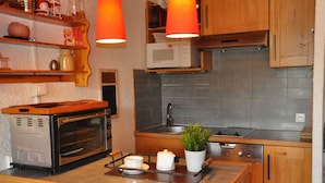 Una cocina con armarios de madera, horno empotrado, microondas, lavabo y una planta en maceta sobre la encimera.