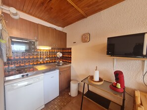 Une cuisine compacte dotée de meubles en bois, d’un four à micro-ondes, d’un four traditionnel, d’un lave-vaisselle, d’un évier, d ’un crédence carrelée, d’une horloge, d’un téléviseur et d’une petite table avec un panier.