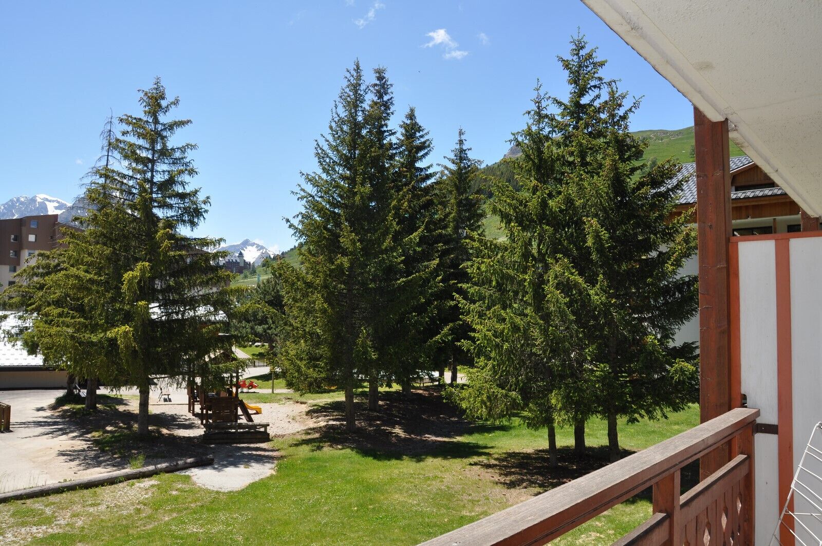 A balcony with a view of a courtyard, trees, and a mountain in the background.