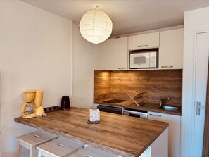Une cuisine dotée d’un plan de travail en bois, de meubles blancs, d’un four à micro-ondes et d’un luminaire suspendu.