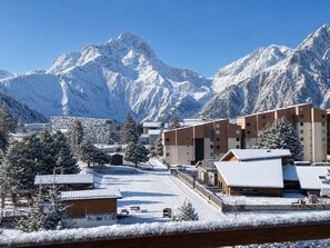 Une station de montagne enneigée, dotée de bâtiments modernes, d’une piste de ski et offrant un ciel dégagé.