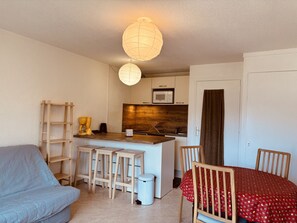 Un espace de vie compact comprenant un coin cuisine, un coin repas avec une table rouge et un canapé.