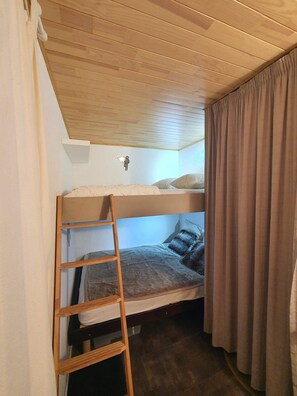 A bunk bed room with a wooden ladder, a small shelf, and a curtain.