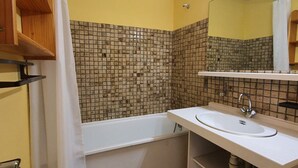 Une salle de bain avec une baignoire, un lavabo, un miroir et des murs carrelés.