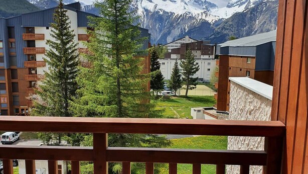 Un balcon avec vue sur des montagnes enneigées, un immeuble doté de balcons et une chaise à rayures jaunes.