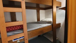 Un lit superposé avec une échelle, une étagère avec une boîte et un oreiller sur le lit du haut.