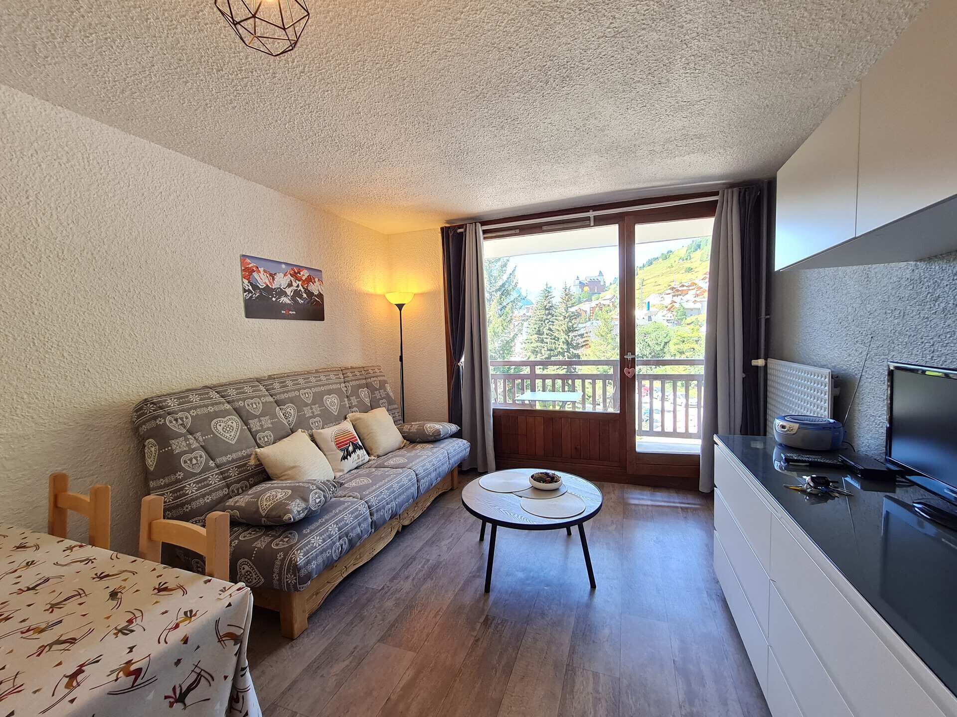 Ein gemütliches Wohnzimmer mit einer Couch, einem kleinen runden Tisch, einem Fernseher und einem Balkon mit Blick.