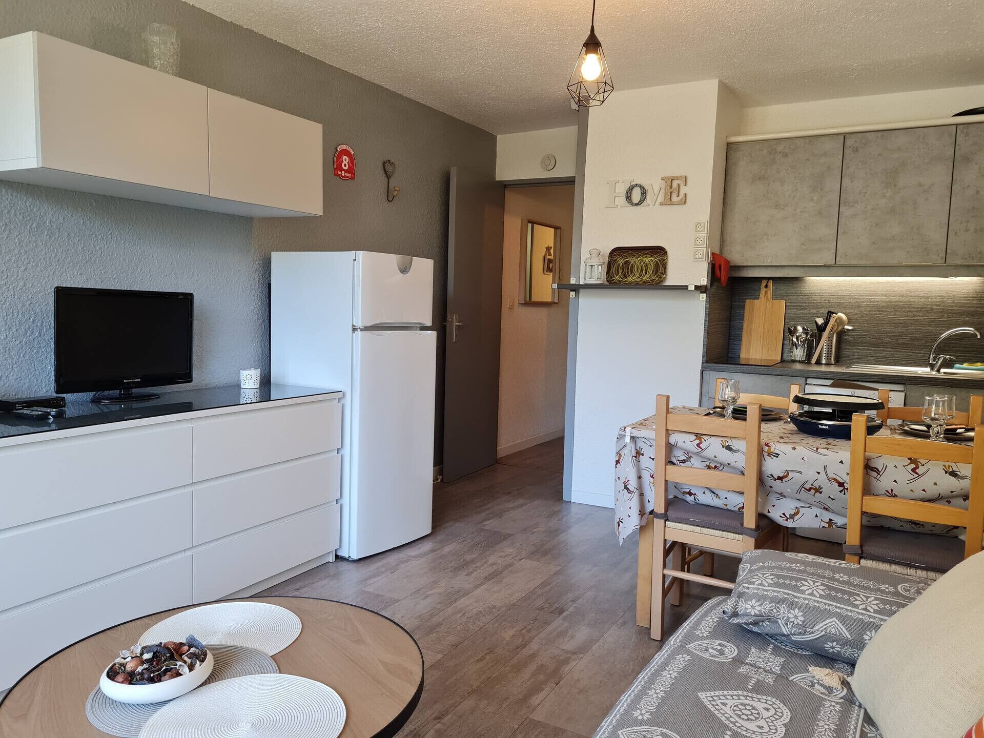 A compact kitchen with a refrigerator, a television, and a dining area with a table and chairs.