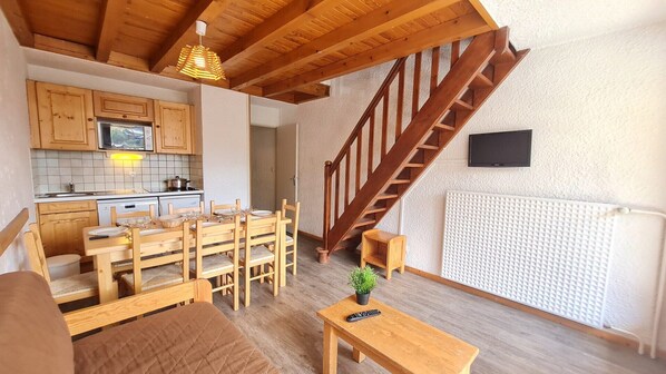 A cozy living space with a wooden staircase, a dining area, and a kitchen. - Spacious duplex 8 ppl, balcony, mountain view (Les Deux Alpes)