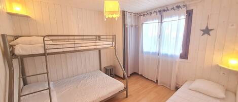 A bunk bed room with a small stool, a window with curtains, and a star decoration on the wall.