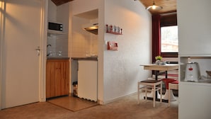 A compact kitchen with wooden cabinets, a microwave, and a small dining area with stools.