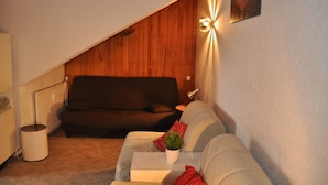 A cozy living room with a sloped ceiling, a dark brown sofa, a light grey sofa, a small white table with a plant, and a wall-mounted light fixture.