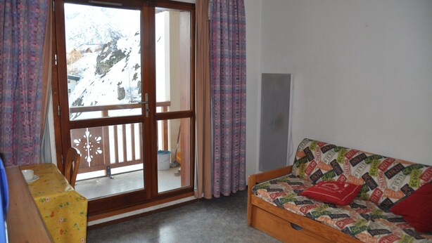 A room with a sliding glass door to a snowy outdoor area, a wooden sofa with patterned upholstery, and a small table with a floral tablecloth. - Studio 3 ppl, balcony, near from the ski station (Les Deux Alpes)