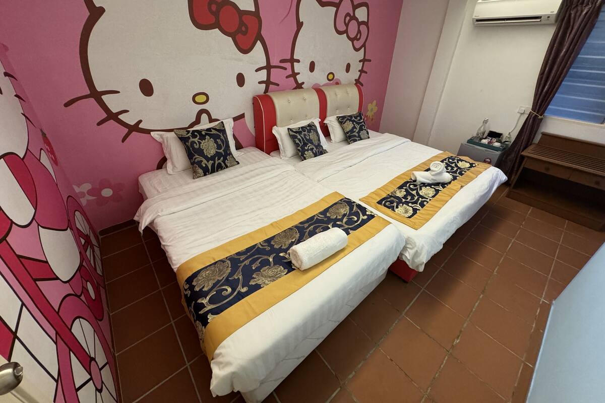 A double bed with floral and striped bedspreads, a headboard with a floral pattern, and a Hello Kitty mural on the wall.