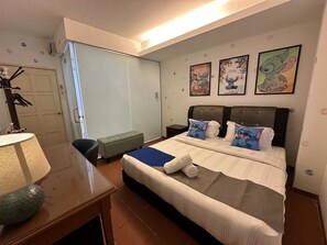 A hotel room with a large bed, a desk with a lamp, a bench, and three wall-mounted pictures. - Dsney Boutique Hotel (Malacca City)