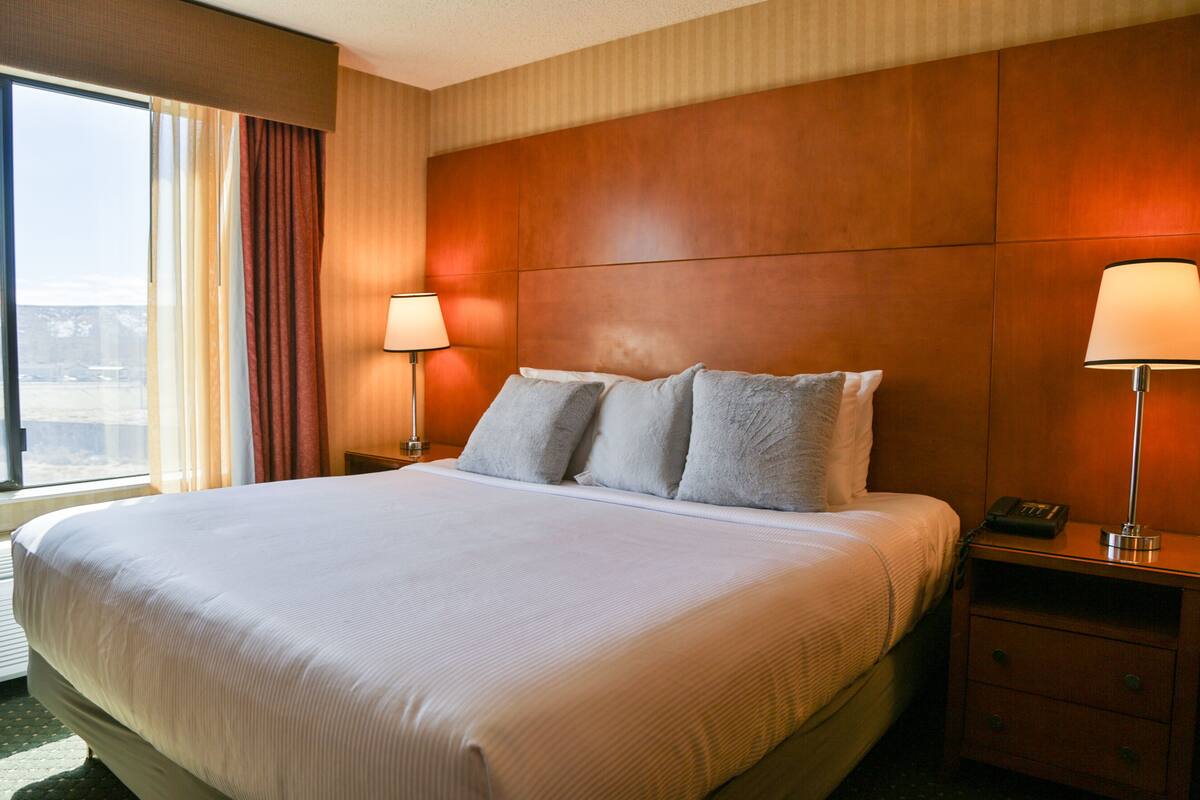 A hotel room with a large bed, two bedside lamps, a nightstand with a phone, and a window with curtains.