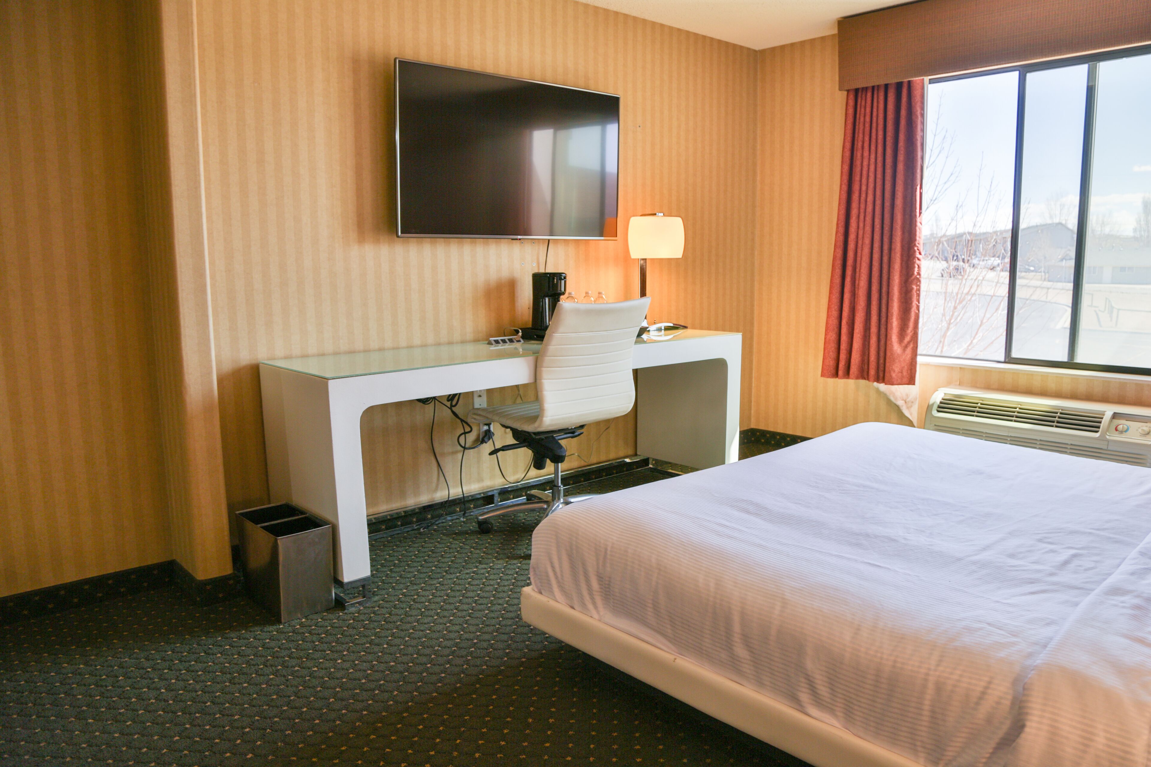 A hotel room with a bed, a desk with a chair, a television, a lamp, and a window with curtains.