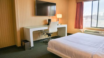 A hotel room with a bed, a desk with a chair, a television, a lamp, and a window with curtains.