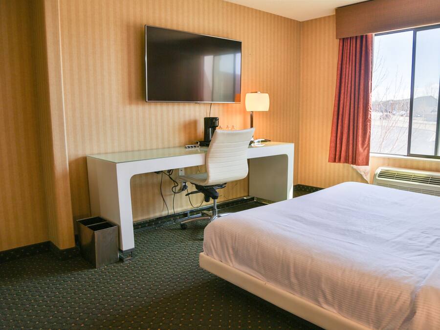 A hotel room with a bed, a desk with a chair, a television, a lamp, and a window with curtains.
