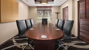A conference room with a large round table, black leather chairs, recessed ceiling lighting, and a large window with blinds. - Sweetwater Lodge (Rock Springs)