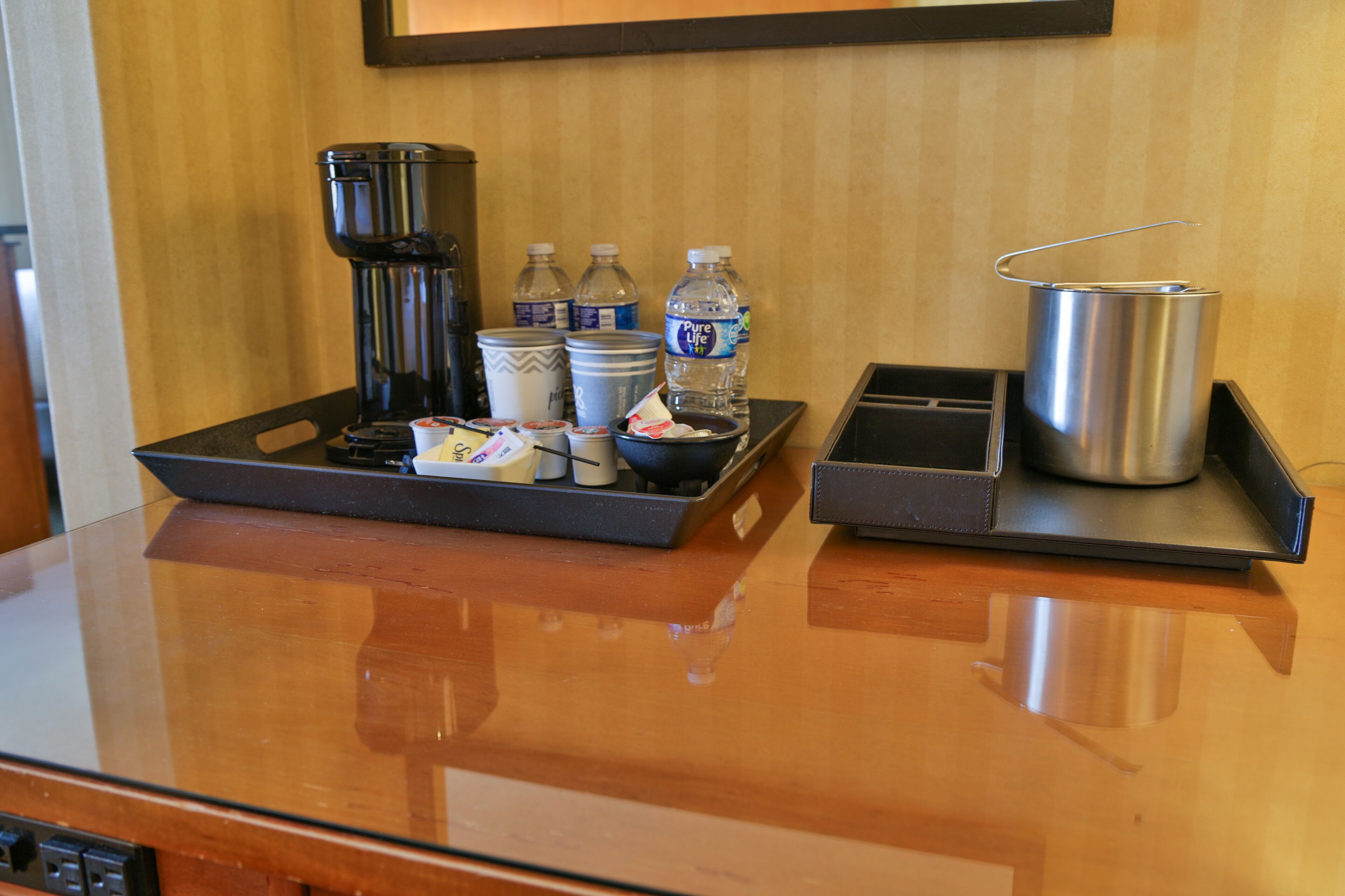 A hotel room's breakfast tray with coffee maker, water bottles, cups, and a silver pot.