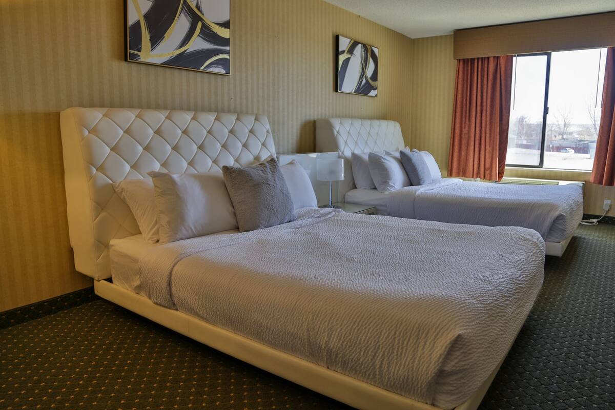 A hotel room with two beds, a large window, and artwork on the walls.