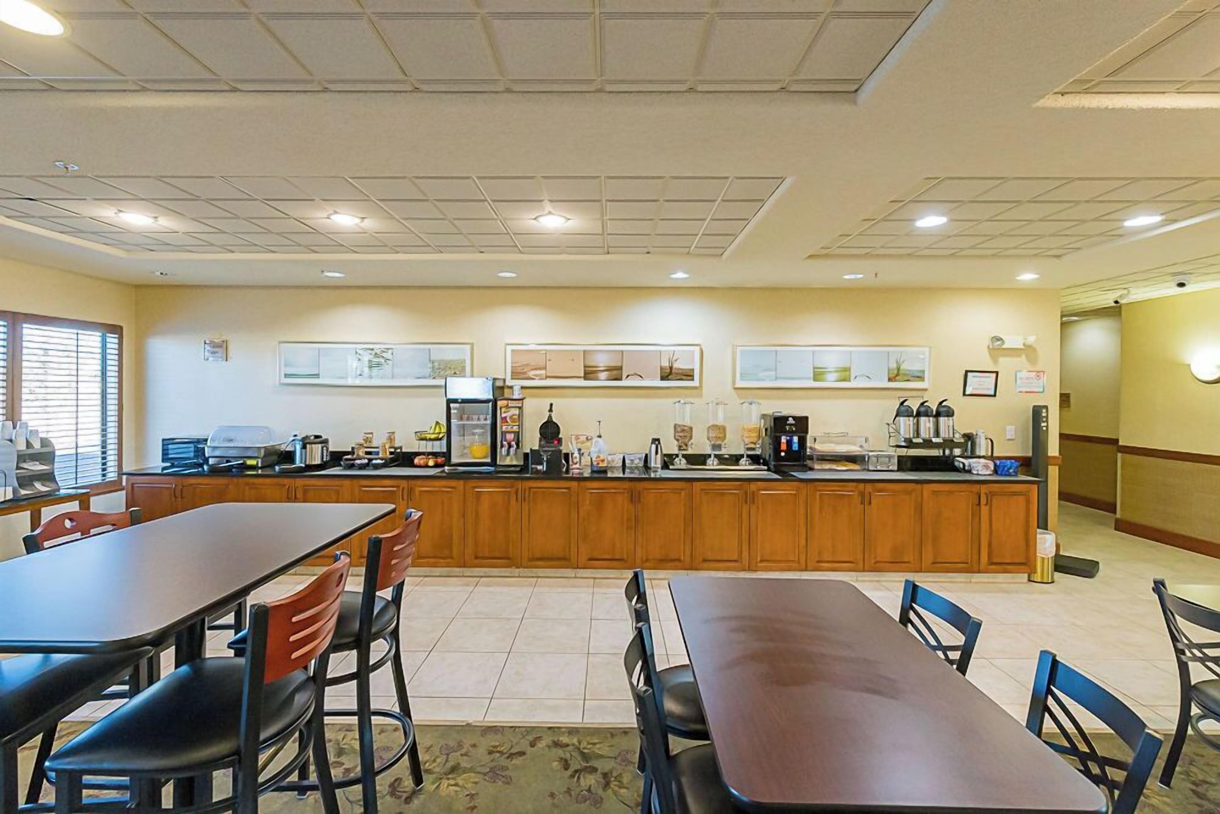 A spacious kitchen with wooden cabinets, a long counter, and various appliances. There are two dining tables with chairs, and artwork is displayed on the walls.