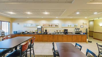A spacious kitchen with wooden cabinets, a long counter, and various appliances. There are two dining tables with chairs, and artwork is displayed on the walls.