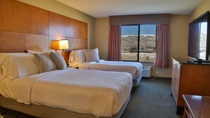 A hotel room with two beds, a desk, a lamp, and a large window with a mountain view. - Sweetwater Lodge (Rock Springs)