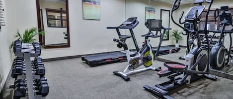 A gym with treadmills, elliptical machines, and a rack of dumbbells.