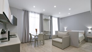 A modern hotel room with a flat-screen TV, a dining area with a table and chairs, a sofa, a bed, and a built-in shelf. - SarMay DeLuxe Apartment ( 2monolocale connected) (bologna)