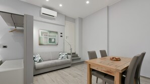A modern, minimalist living room with a grey sofa, a wooden dining table, and a staircase. - SarMay DeLuxe Apartment ( 2monolocale connected) (bologna)