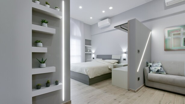 A modern bedroom with a bed, bedside tables, a sofa, and built-in shelves with plants. - SarMay DeLuxe Apartment ( 2monolocale connected) (bologna)