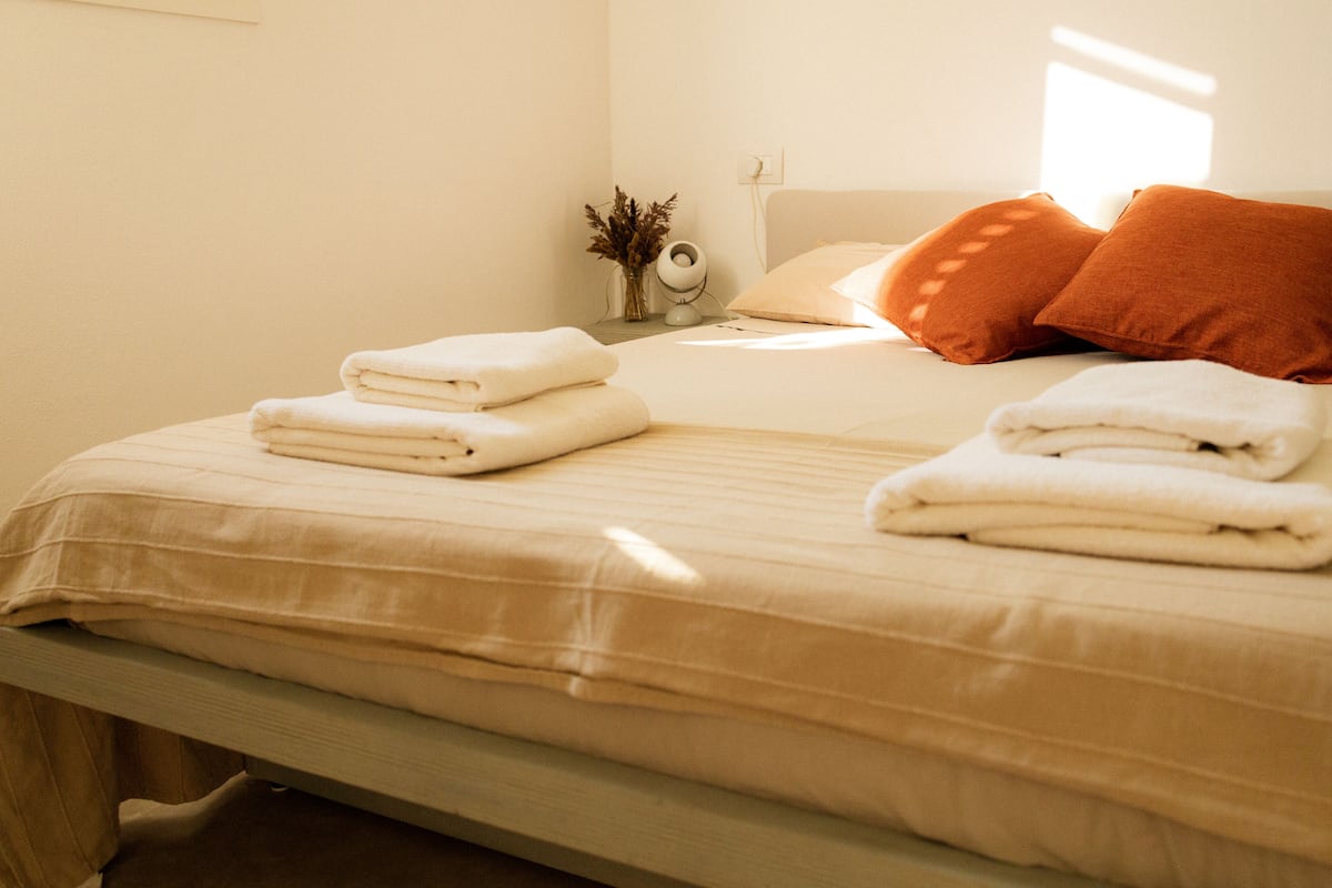 Un lit bien fait, avec des serviettes pliées et deux oreillers orange.